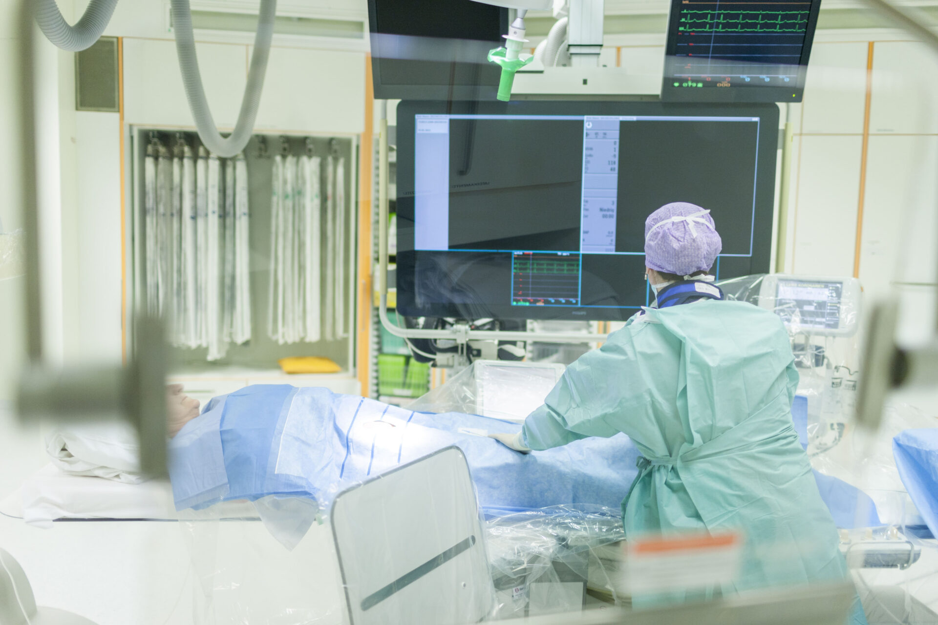 am Bild wird ein Mitarbeiter gezeigt, der gerade eine CAG-Untersuchung am Patienten durchführt (Herzkatheter)