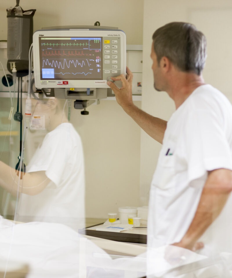 Die DGKP sieht sich die Zahlen am Monitor an, welcher beim Patienten angeschlossen ist