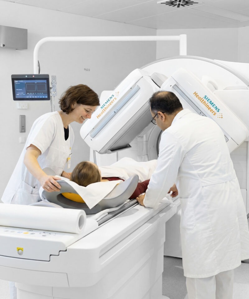 der behandelnde Arzt und die Radiologietechnologin richten die Patientin für die Gammakamera-Untersuchung beim PET-/SPECT-Gerät ein