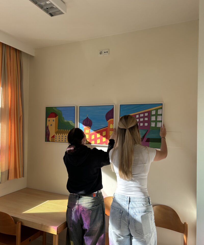 zwei Schülerinnen hängen ein von ihnen gemaltes Bild auf der Psychiatrie-Station auf