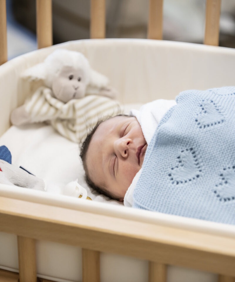 das Neugeborene liegt im Beistellbett liebevoll in warmen Decken eingehüllt