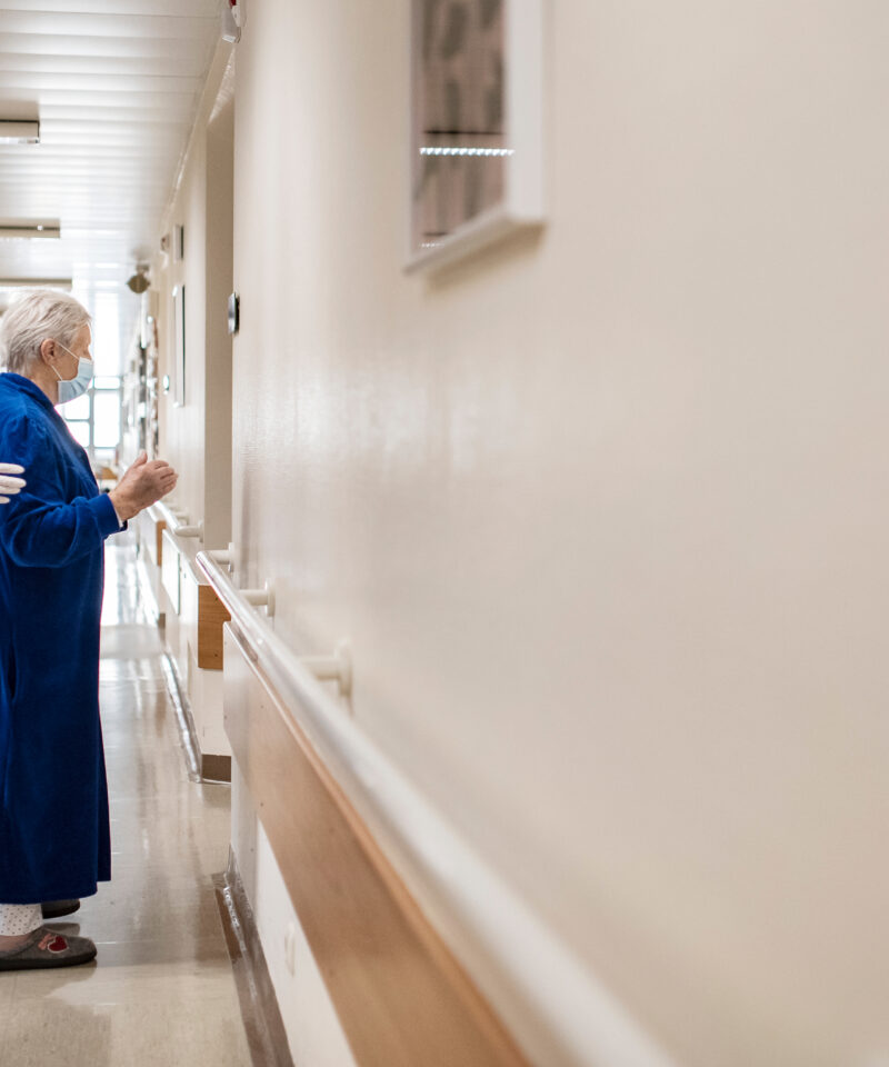eine Pflegekraft hilft einer betagten Patientin zurück ins Patientenzimmer