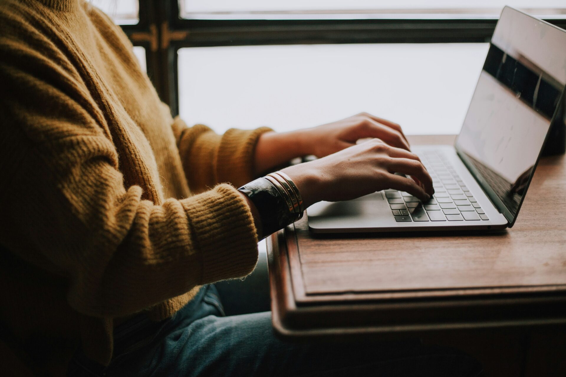 eine Person sitzt an einem Tisch und tippt am Laptop